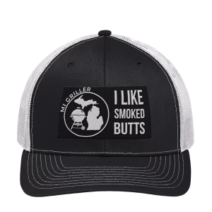 Front view of the black MI Griller Trucker Hat featuring white embroidered text reading "I LIKE SMOKED BUTTS" next to the circular MI Griller kettle and Michigan silhouette logo on a structured front panel.